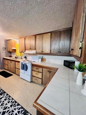 A kitchen with wooden cabinets, a stove, a microwave, and a sink. - Rachel's Place (Vicksburg)