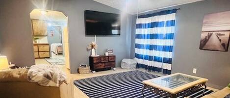 A living room with a ceiling fan, a TV mounted on the wall, a striped rug, and a sofa.