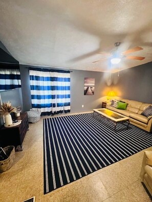 A living room with a sofa, a coffee table, a striped rug, and a ceiling fan. - Rachel's Place (Vicksburg)
