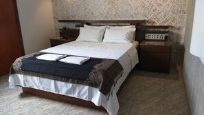 A neatly made bed with a patterned bedspread, a bedside table with a phone, and a power outlet on the wall. - Hotel Millennium (São Paulo)