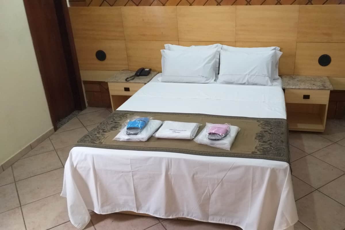A hotel room with a bed, two bedside tables, a telephone, and a table with towels and a phone.