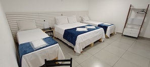 A room with three beds, each with white bedding and blue accents, a wooden nightstand, a small table, and a wooden chair. - Hotel Millennium (São Paulo)