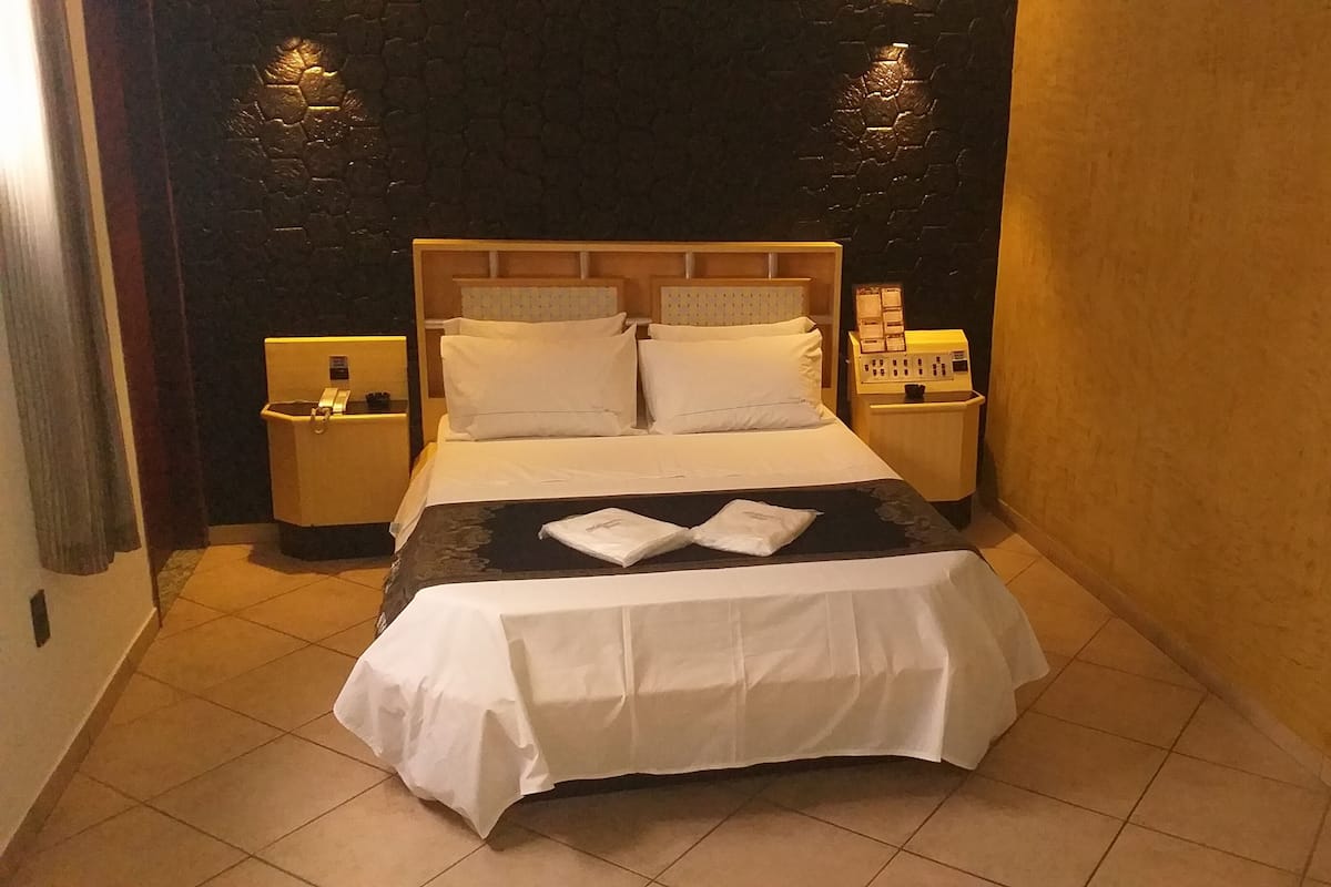 A neatly made bed with white linens and a black and white throw blanket, two bedside tables with lamps, and a dark textured wall.