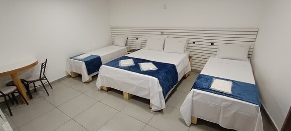 A hotel room with three single beds, a small table with chairs, and a plain white wall. - Hotel Millennium (São Paulo)
