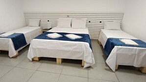 Habitación de hotel con tres camas individuales, cada una con cubrecama blanco y azul, y cabecero de madera.