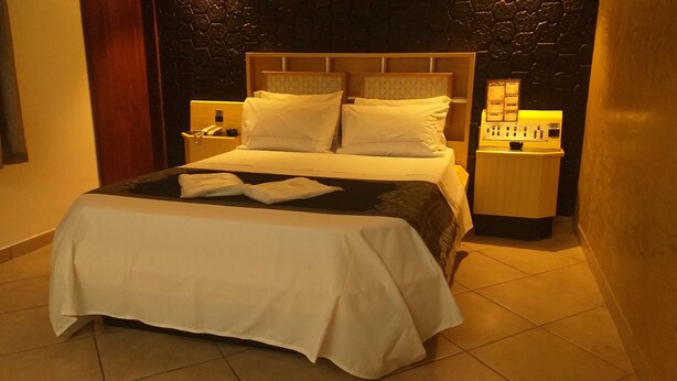 Una cama bien hecha con ropa de cama blanca, un cabecero de madera y dos mesitas de noche con lámparas.