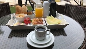 Una bandeja de desayuno con pan, bollería, fruta y una taza de café sobre una mesa de vidrio.