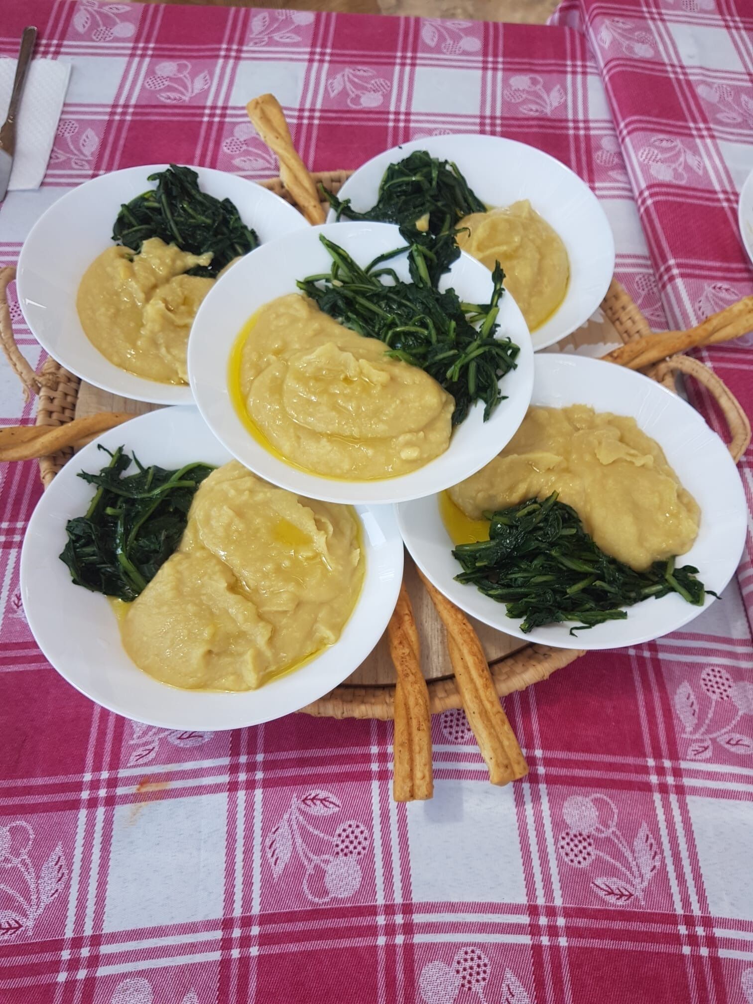 Four white plates with yellowish food and green leafy vegetables, arranged on a pink and white checkered tablecloth.