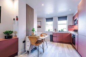 Een moderne keuken met een eetgedeelte, met een houten eettafel, rieten stoelen en een inbouwoven.