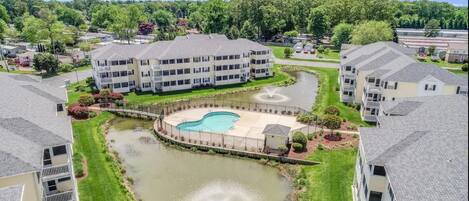 A residential complex with a central swimming pool, multiple buildings, and a landscaped area with fountains.