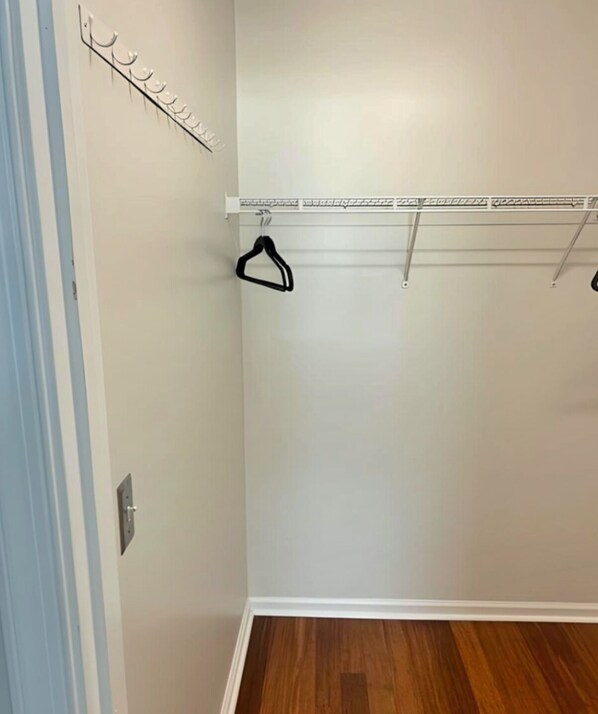 A closet with a wooden floor, white walls, and a metal hanging rod with hooks. - Coastal Oasis - Cozy 2BR Condo in Rehoboth Beach (Rehoboth Beach)