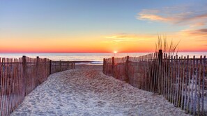 A sandy beach path leading to the ocean with a sunset in the background. - Coastal Oasis - Cozy 2BR Condo in Rehoboth Beach (Rehoboth Beach)