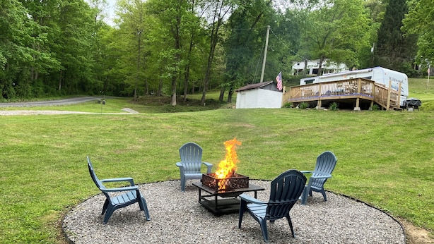 A circular outdoor seating area with a fire pit, surrounded by chairs, in a grassy yard with a deck and a house in the background.