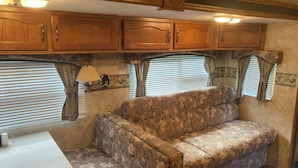 A compact RV interior with a sofa, wooden cabinets, a table, and a lamp.