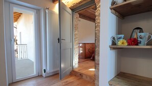 A wooden floor, a white door, a stone wall, and a shelf with mugs and flowers. - Baita Tersilia Near Lake And Mountain  (Borgo Valbelluna)