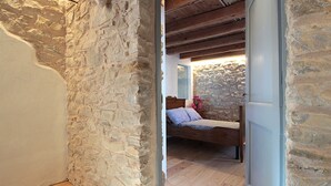 A room with a stone wall, wooden floor, and a bed with a wooden headboard. - Baita Tersilia Near Lake And Mountain  (Borgo Valbelluna)