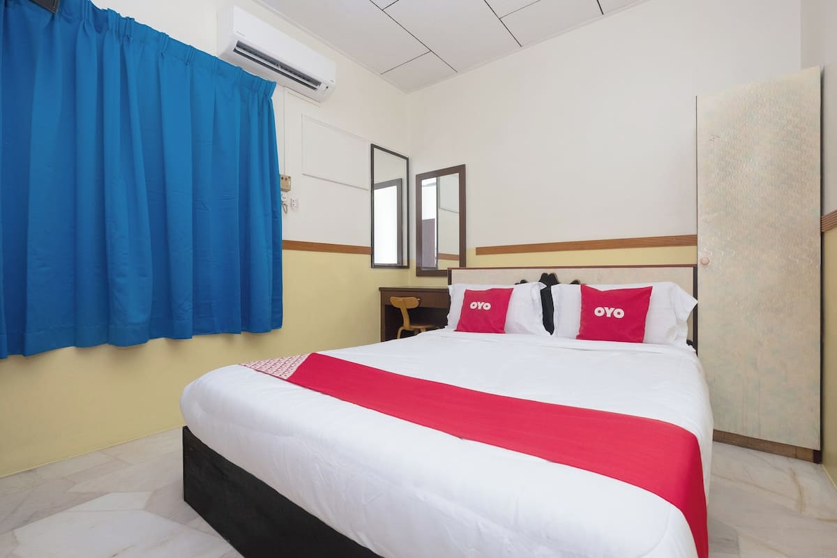 A hotel room with a bed, blue curtains, two mirrors, and a red and white bedspread.