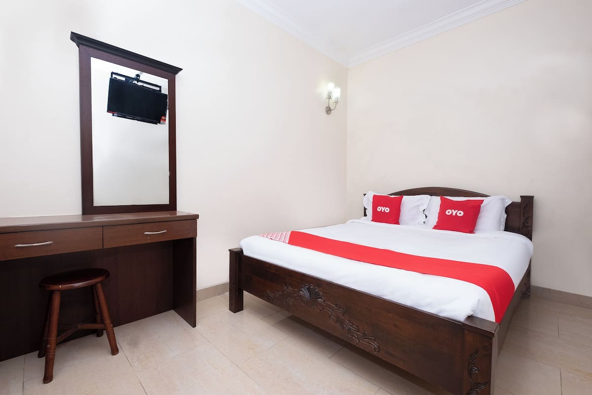 A bedroom with a wooden bed, a desk with drawers, a stool, and a mirror.