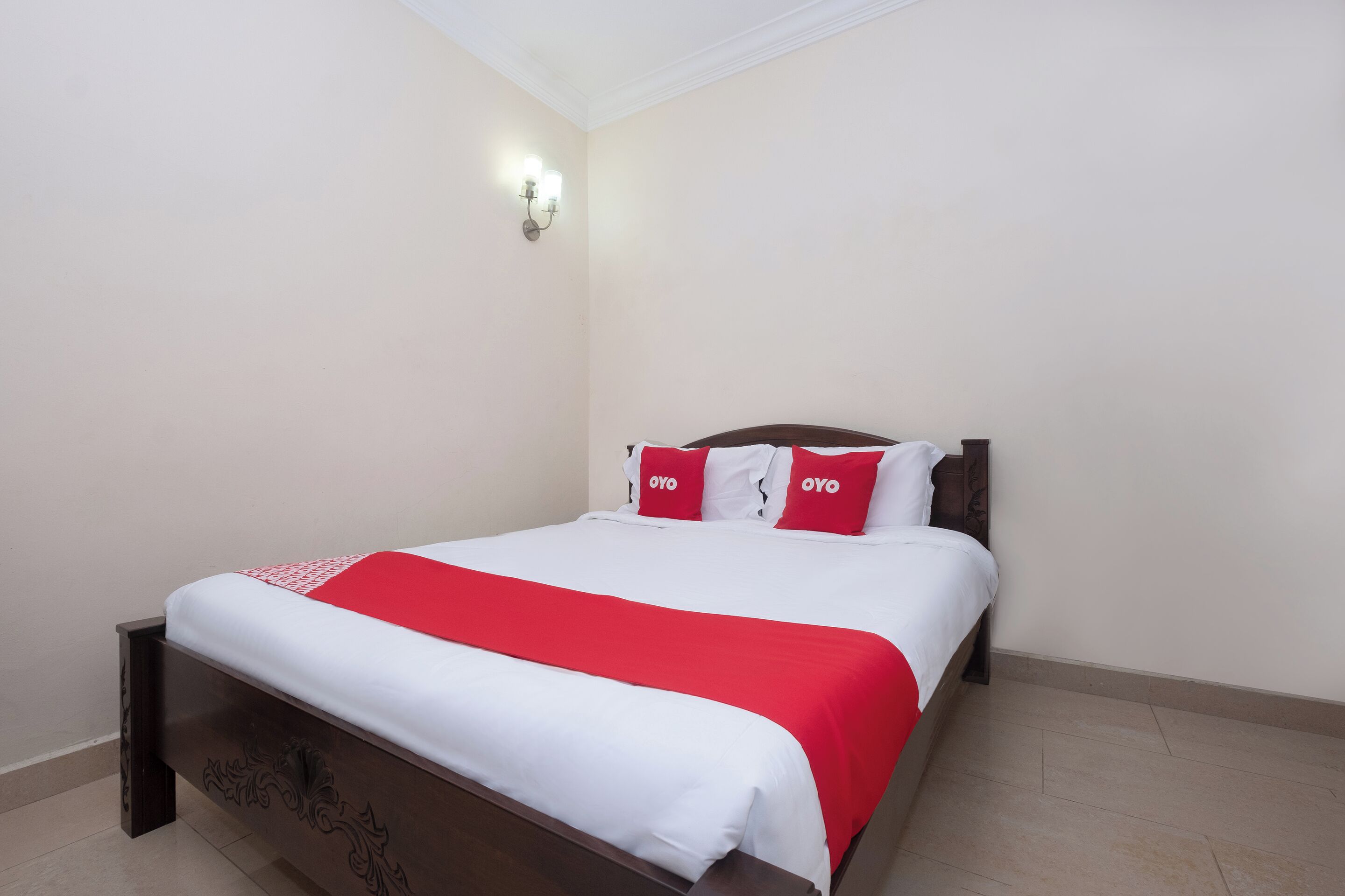 A neatly made bed with a white and red bedspread, a wooden headboard, and a wall-mounted light fixture.