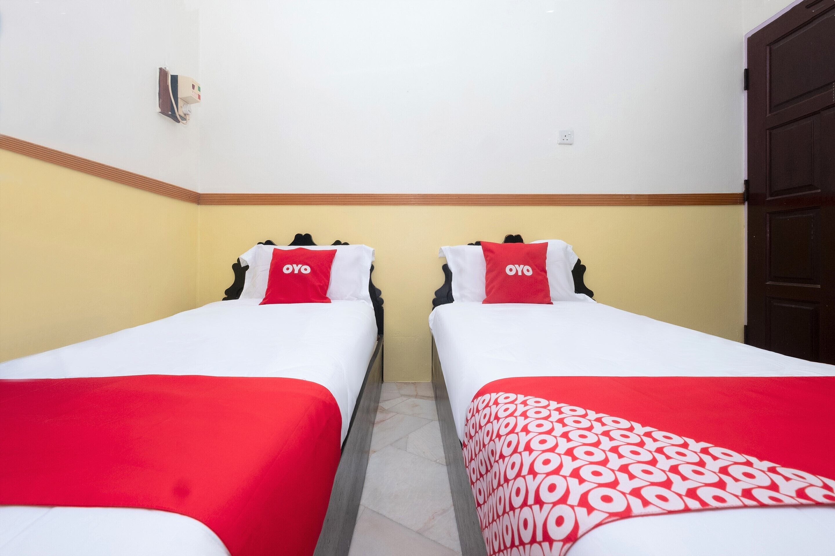 Habitación de hotel con dos camas, cada una con una colcha y almohadas rojas y blancas, y una manta roja y blanca estampada.