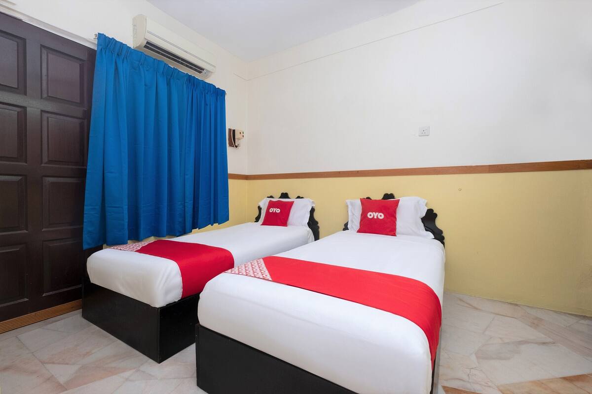 A hotel room with two beds, each with white bedding and red accents, a closed dark wooden door, and a blue curtain.