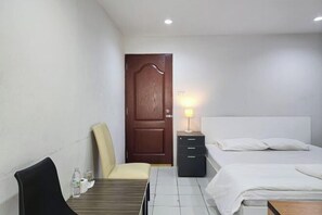 A hotel room with a bed, bedside table, lamp, chair, and a small table with toiletries. - Freesia Bangphi Guest House (Bang Phli)