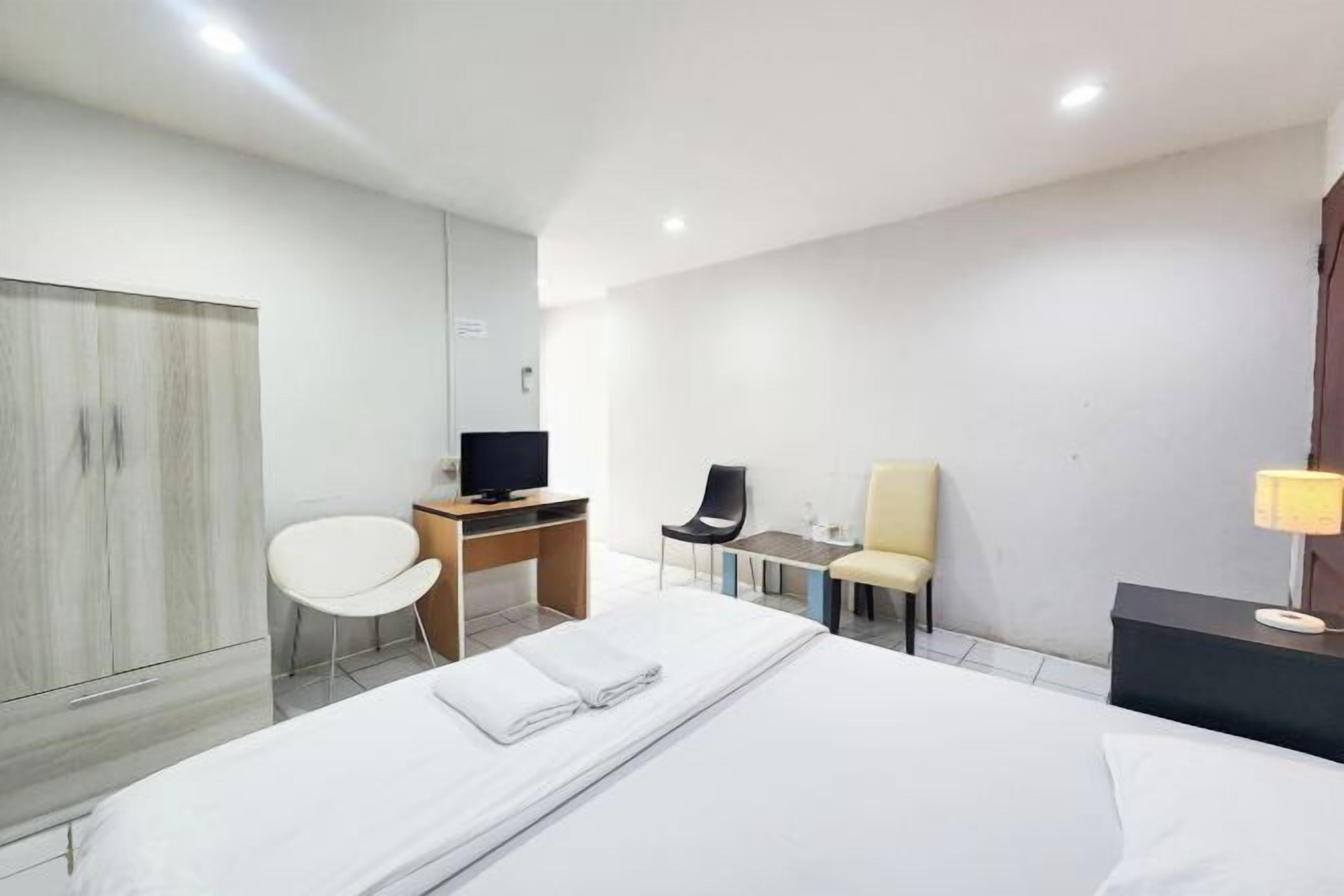 Une chambre d’hôtel équipée d’un lit, d’un bureau avec un ordinateur, d’une chaise, d’une télévision et d’une lampe.