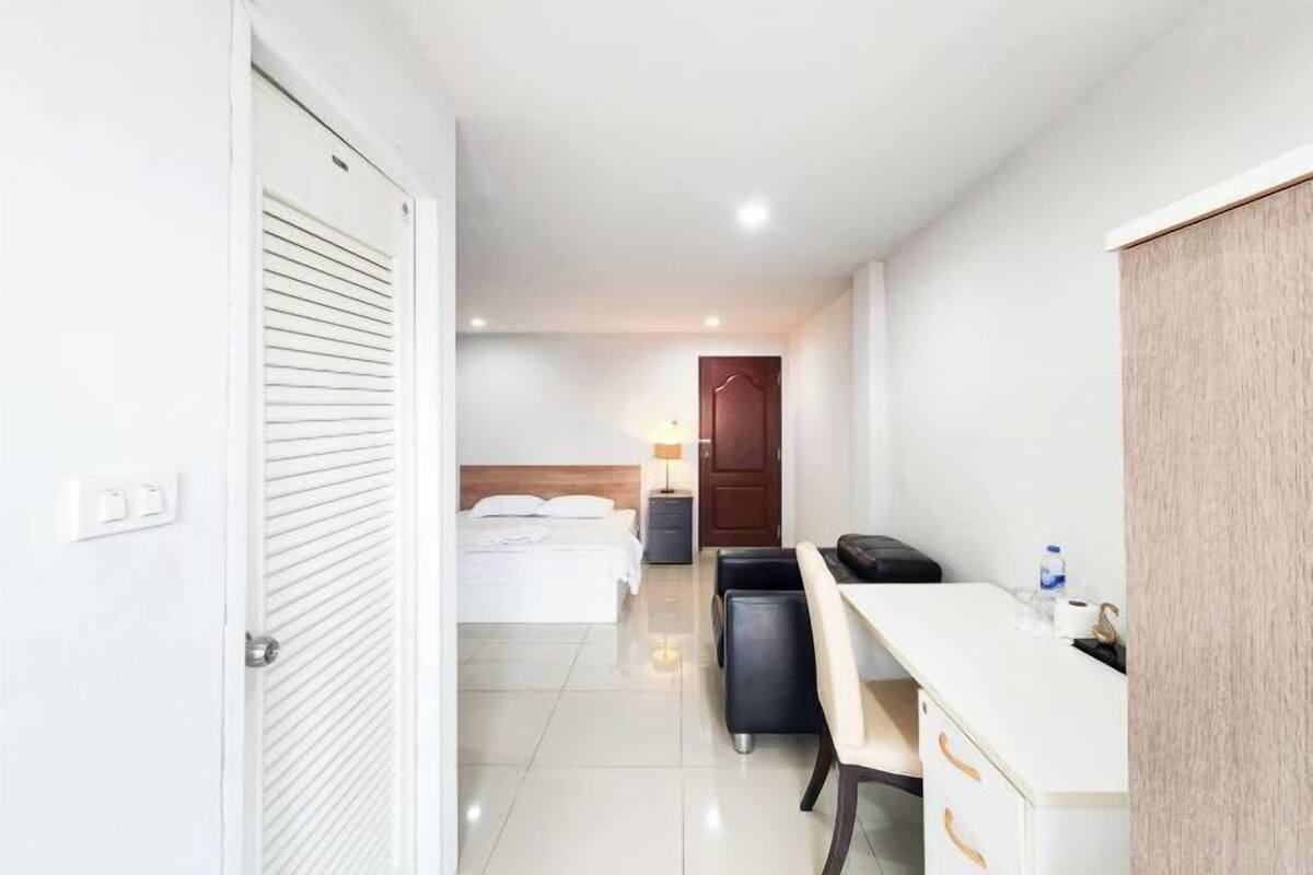 A hotel room with a bed, a desk, a chair, a wardrobe, and a bedside table.