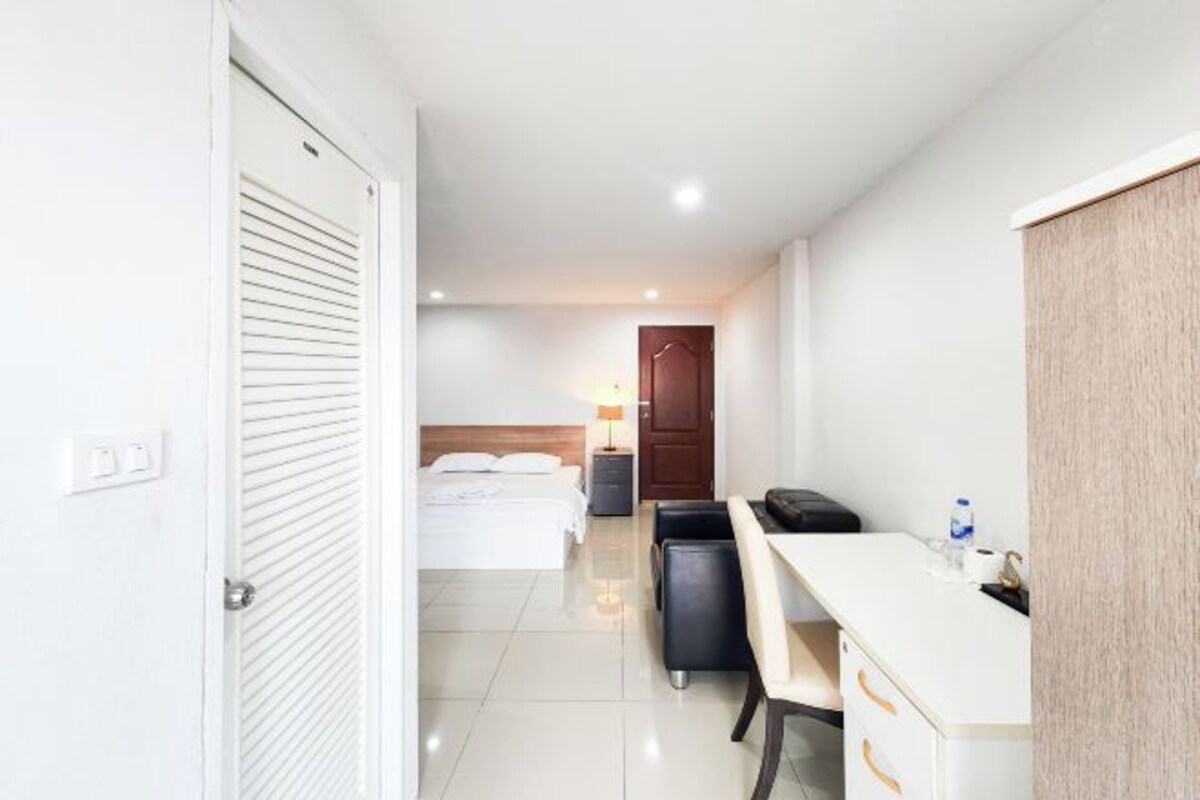 A hotel room with a bed, desk, chair, and a small table with a lamp.