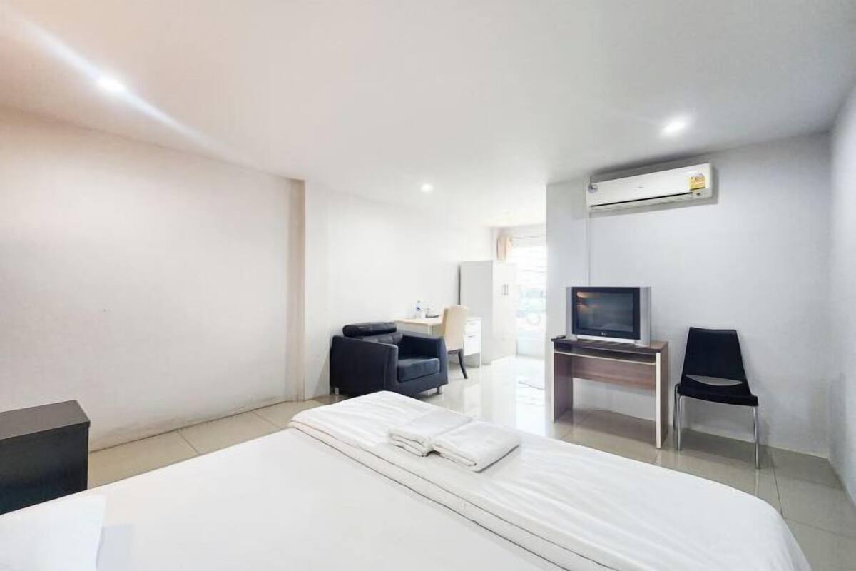 A hotel room with a bed, a desk, a chair, a television, and an air conditioning unit.