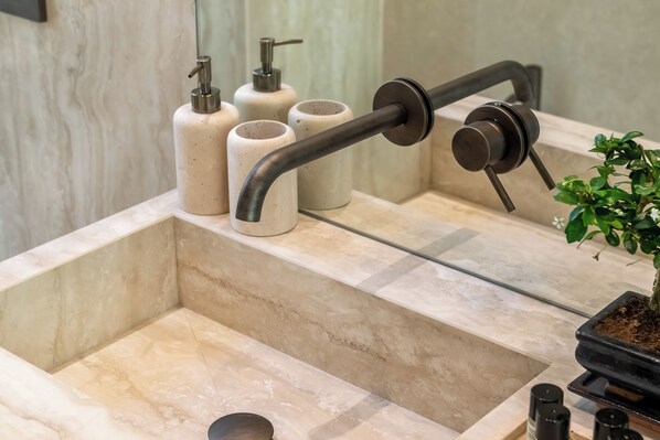Un baño con lavamanos de mármol, grifo negro y una planta en maceta.
