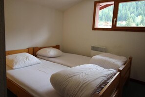 Een kleine, eenvoudige kamer met twee eenpersoonsbedden, een raam met uitzicht op een bos en een wandradiator.