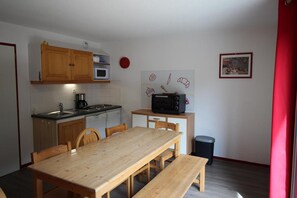 A compact kitchen with wooden cabinets, a microwave, and a dining table with benches. - 70m from ski slopes, 7th floor, balcony, parking, tv, ski locker, 62m², Valfréjus (Valfréjus)