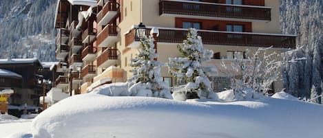 A multi-story hotel with balconies, snow-covered trees, and a mountainous backdrop.