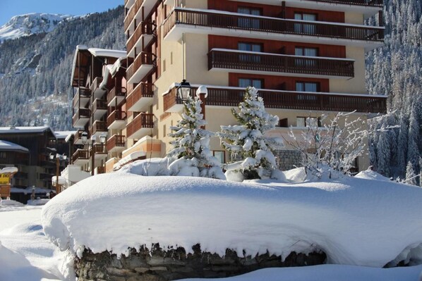 A multi-story hotel with balconies, snow-covered trees, and a mountainous backdrop.