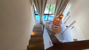 Eine Treppe mit Holzboden und Metallgeländer, die zu einem Raum mit einem großen Fenster, Vorhängen und einer Hängelampe führt.