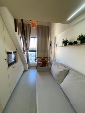 A modern living room with a sofa, a dining table, and a staircase. - Duplex Vista Piscina by La Playa (Ipojuca)