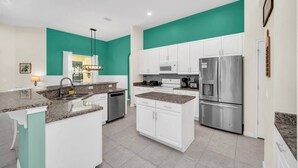 A modern kitchen with white cabinets, a granite countertop, stainless steel appliances, and teal accent walls.