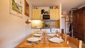 Een eettafel gedekt met borden, glazen en bestek, houten kasten, een magnetron en een betegelde achterwand in een keuken.