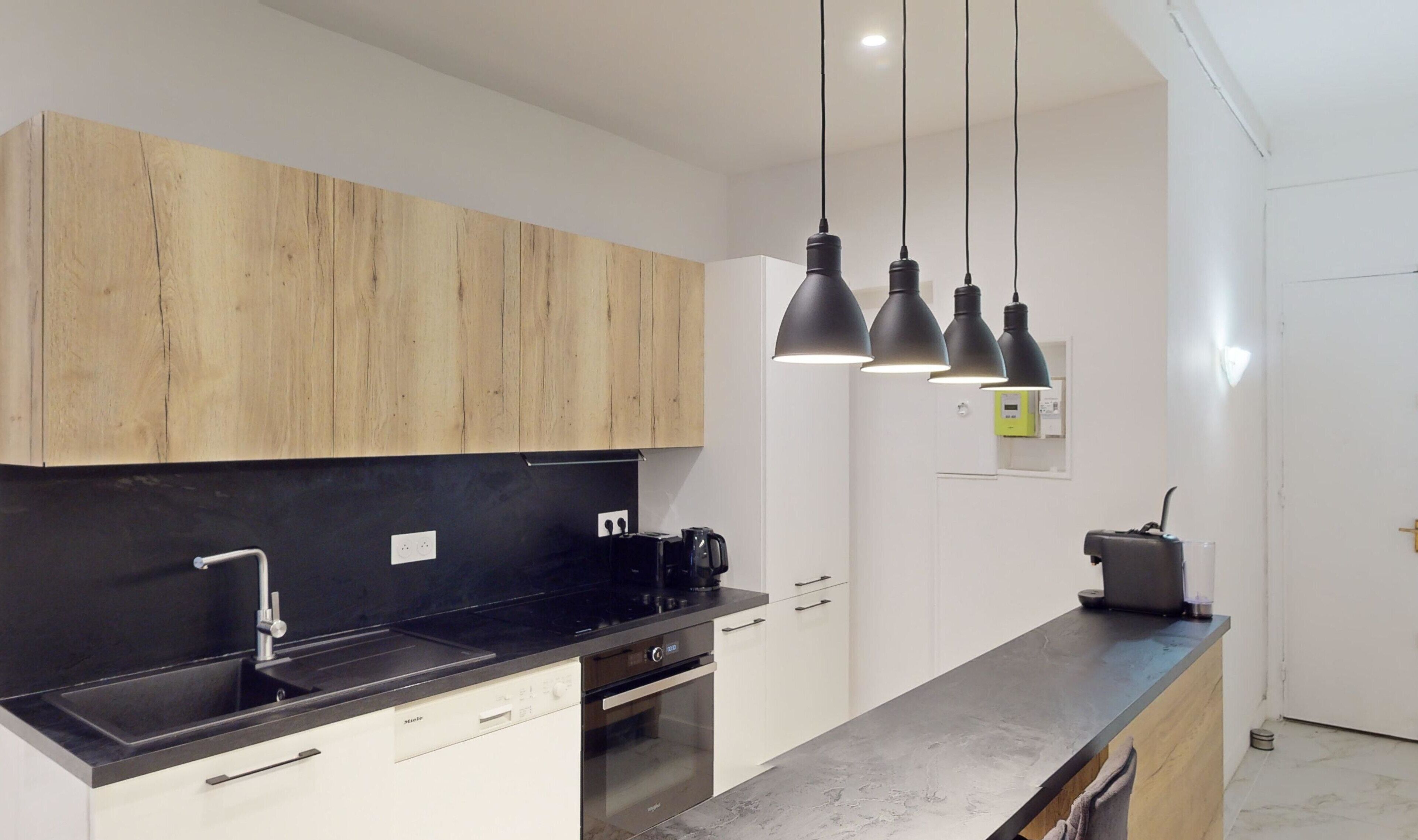 A modern kitchen with wooden cabinets, a black countertop, a built-in oven, and pendant lights.