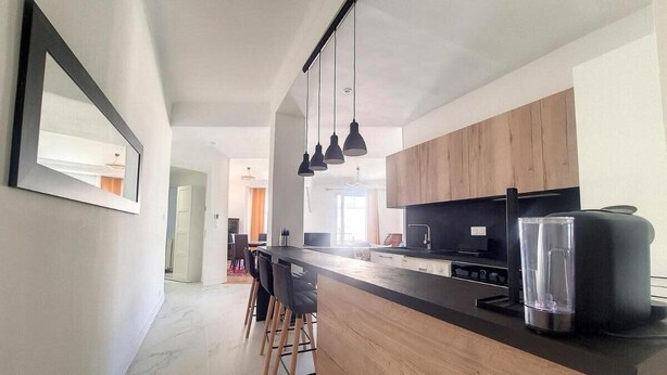 A modern kitchen with a central island, pendant lighting, and a view into the dining area. - Bright air-conditioned flat in the city centre (Nice)