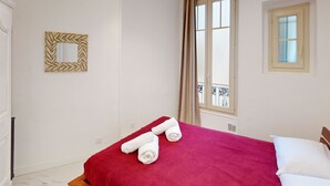 A hotel room with a bed, a window with curtains, a wall-mounted mirror, and a small balcony visible through the window. - Bright air-conditioned flat in the city centre (Nice)