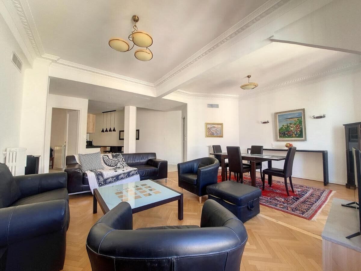 A spacious living room with black leather sofas, a coffee table, and a dining area with a table and chairs.