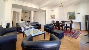 A spacious living room with black leather sofas, a coffee table, and a dining area with a table and chairs. - Bright air-conditioned flat in the city centre (Nice)
