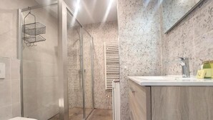 A modern bathroom with a glass shower enclosure, a white toilet, and a wooden vanity with a mirror. - Bright air-conditioned flat in the city centre (Nice)