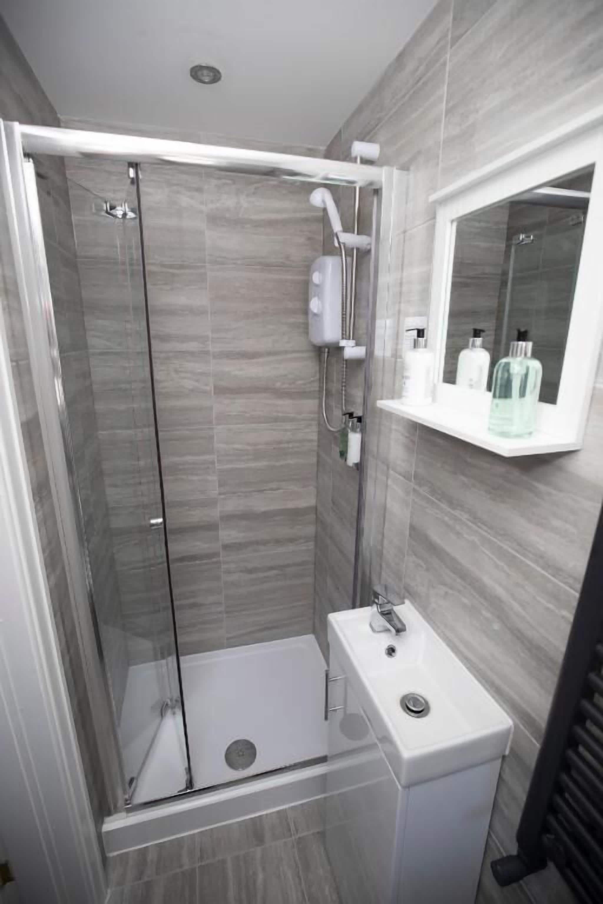 A modern bathroom with a glass-enclosed shower, a white sink, and a mirror above it.