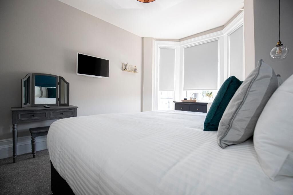 A bedroom with a large bed, a dresser, a television, and a window with curtains.