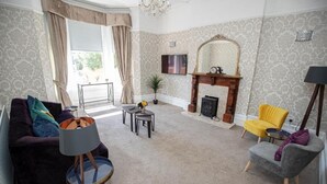 Een woonkamer met een bank, fauteuils, een salontafel, een open haard en een televisie.