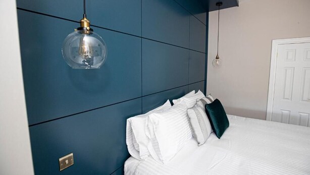 Een slaapkamer met een bed, witte beddengoed, een blauwe accentmuur en een hangende lamp.