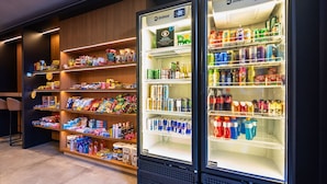 Two Imbéra refrigerators stocked with beverages and snacks, surrounded by shelves of various food items. - STAY Urbà Home (Goiania)